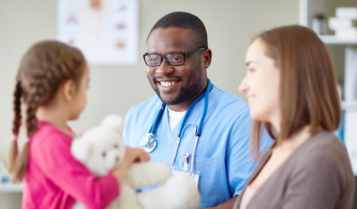 Family medicine doctor smiles at a toddler and her mother during a check-up visit