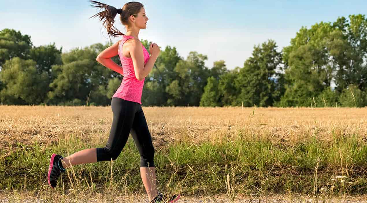 woman—who is jogging near farmland—wears proper footwear to avoid common running injuries